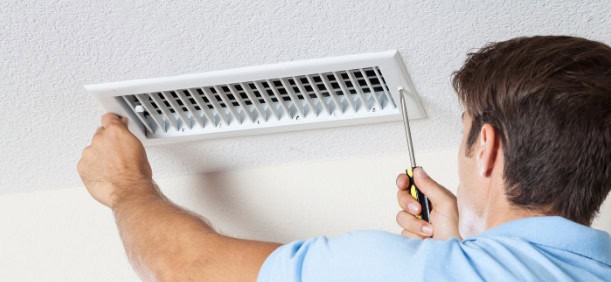 A photo of a man servicing a ducted air conditioner vent.
